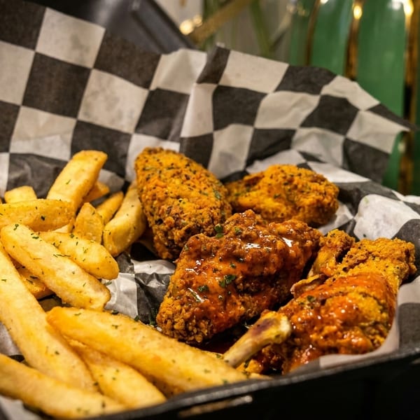 Seasoned french fries and sauced chicken wings in a black and white checkered basket.