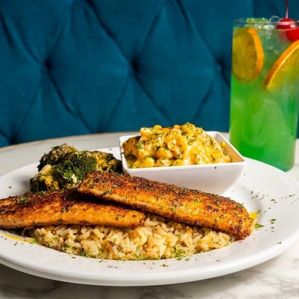 Seasoned salmon, rice, broccoli, mac and cheese, and a green cocktail on a marble table.